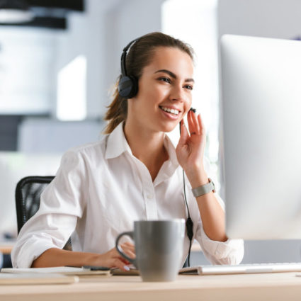 Image of a happy emotional business woman in office callcenter working with computer wearing headphones.